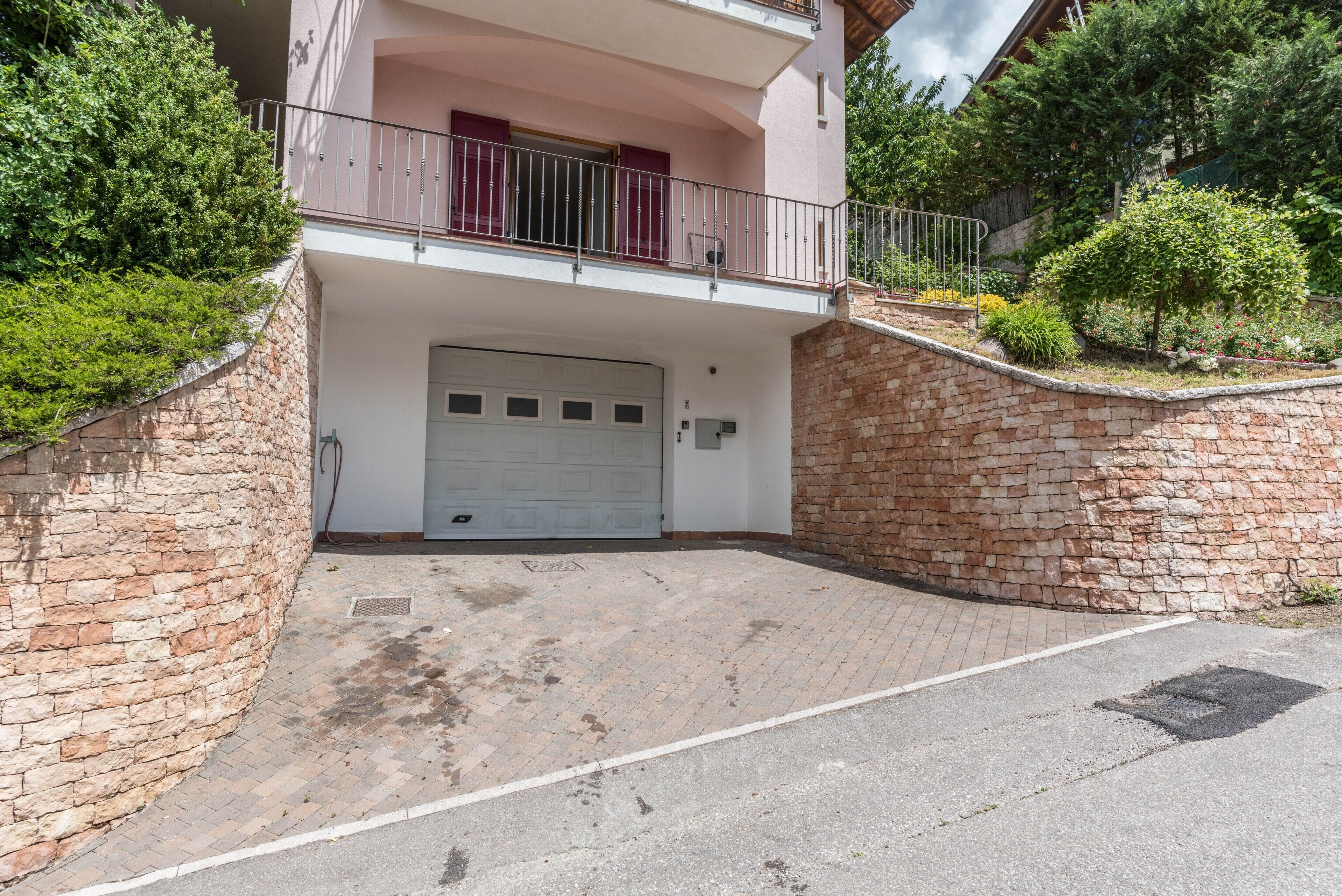 A two-story building with a garage, stone walls, and a balcony with metal railings.