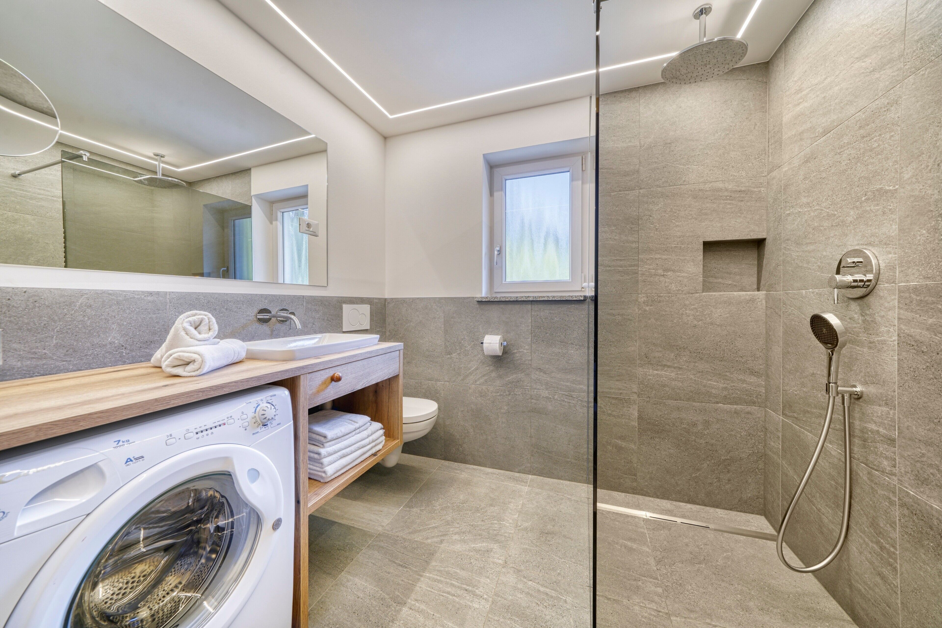 Un baño moderno con lavadora, inodoro, ducha y ventana.