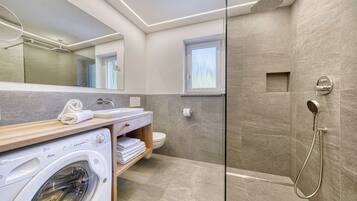 Un baño moderno con lavadora, inodoro, ducha y ventana.