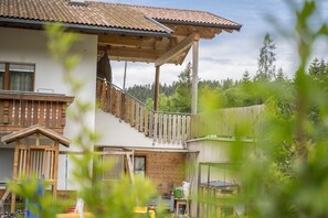 Une maison à deux étages dotée d’un balcon en bois, d’une terrasse en bois et offrant une vue sur une zone boisée.