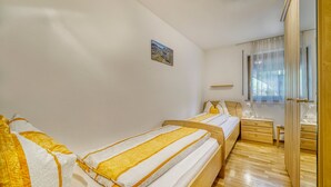 Ein Schlafzimmer mit zwei Betten, Holzböden, einem Nachttisch, einem Spiegel und einem Fenster mit Vorhängen.