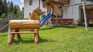 A wooden play structure with a slide, a wooden swing set, and a small wooden building with a balcony. - Holiday Apartment "Boznermüllerhof-Sonnenblume" with Balcony and View into Nature (Vöran)