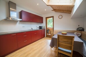 A modern kitchen with red cabinets, a stainless steel range hood, and a dining area with a wooden table and chairs.