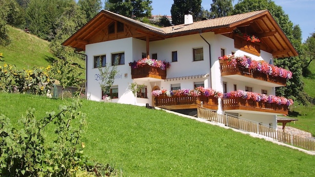 A two-story building with balconies adorned with flowers, surrounded by greenery and trees. - Holiday Apartment "Boznermüllerhof-Sonnenblume" with Balcony and View into Nature (Vöran)