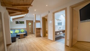 A modern interior with a wooden ceiling, a sofa with cushions, a small table, and a kitchen area visible through an open door. - Holiday Apartment "Boznermüllerhof-Sonnenblume" with Balcony and View into Nature (Vöran)