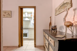 A hallway leading to a kitchen with a wooden door, a decorative giraffe, and a zebra lamp on a dresser.