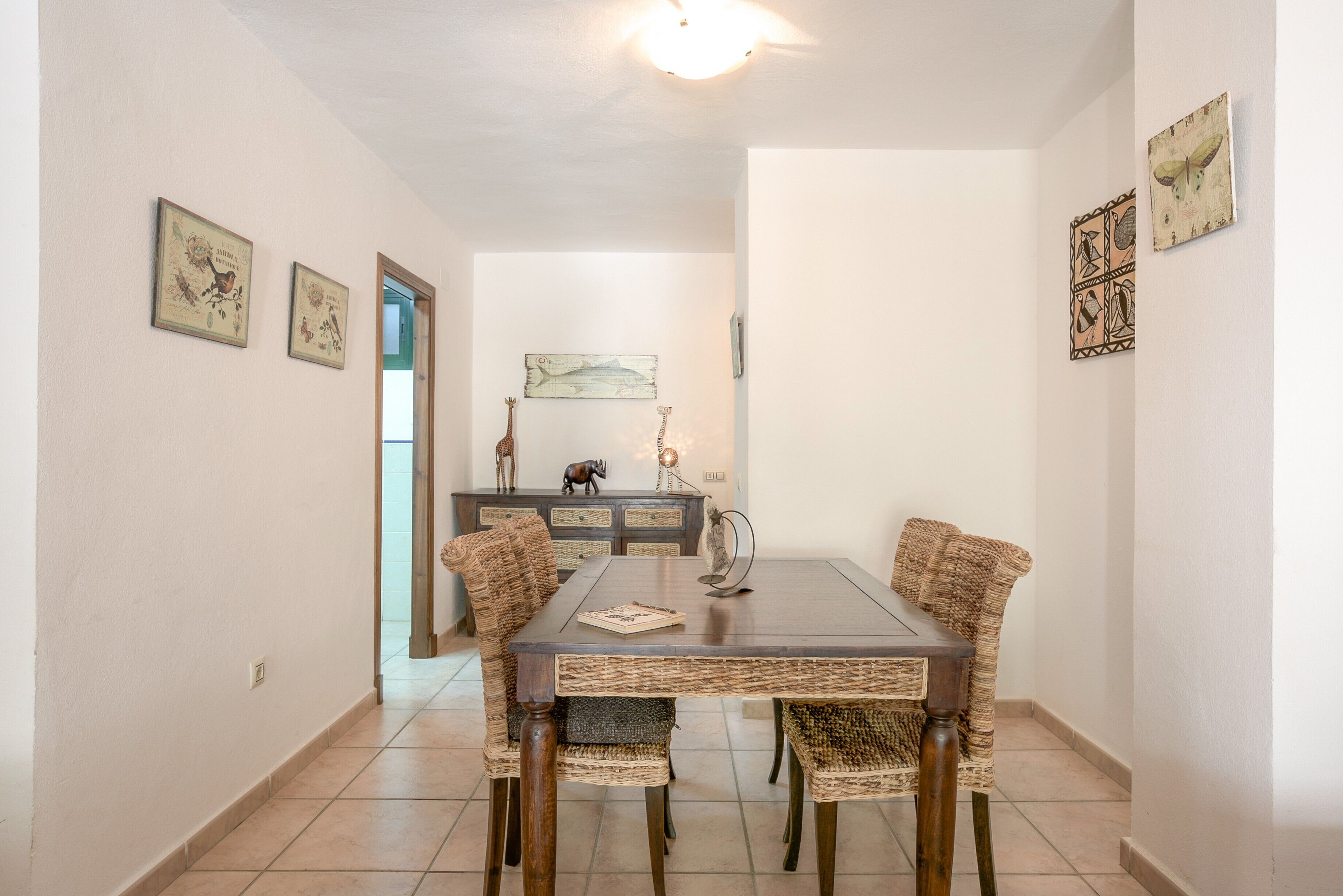 A dining area with a dark wooden table and wicker chairs, a decorative cabinet with figurines, and wall art.