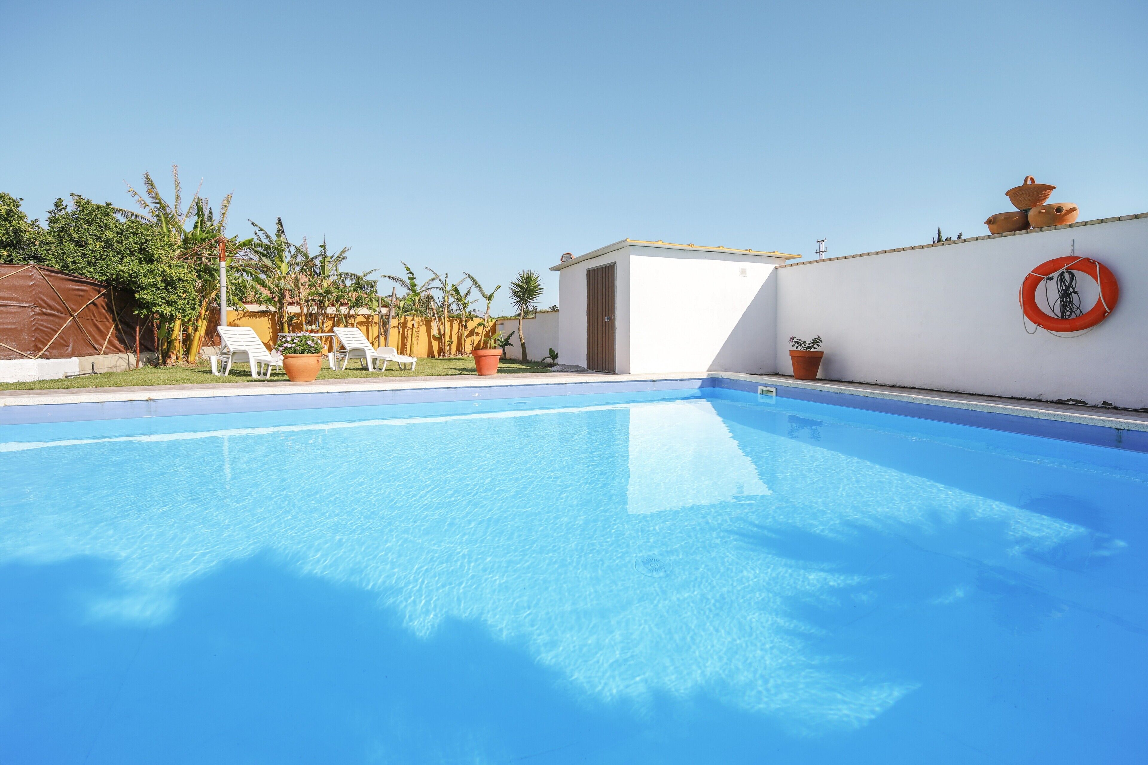 A clear blue swimming pool with white lounge chairs and potted plants.