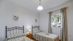 Un dormitorio con dos camas, una mesita de noche con lámpara y una ventana con cortinas.