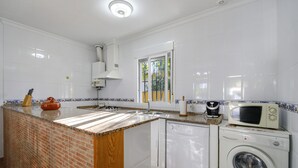 Una cocina con armarios blancos, microondas, lavavajillas, fregadero y ventana.