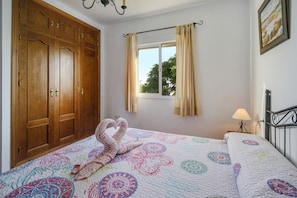 Een slaapkamer met een grote houten garderobe, een raam met gordijnen, een bed met een geborduurde sprei en een wandlamp.