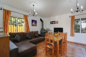 Een woonkamer met een bank, eettafel, stoelen, een televisie en een open haard.