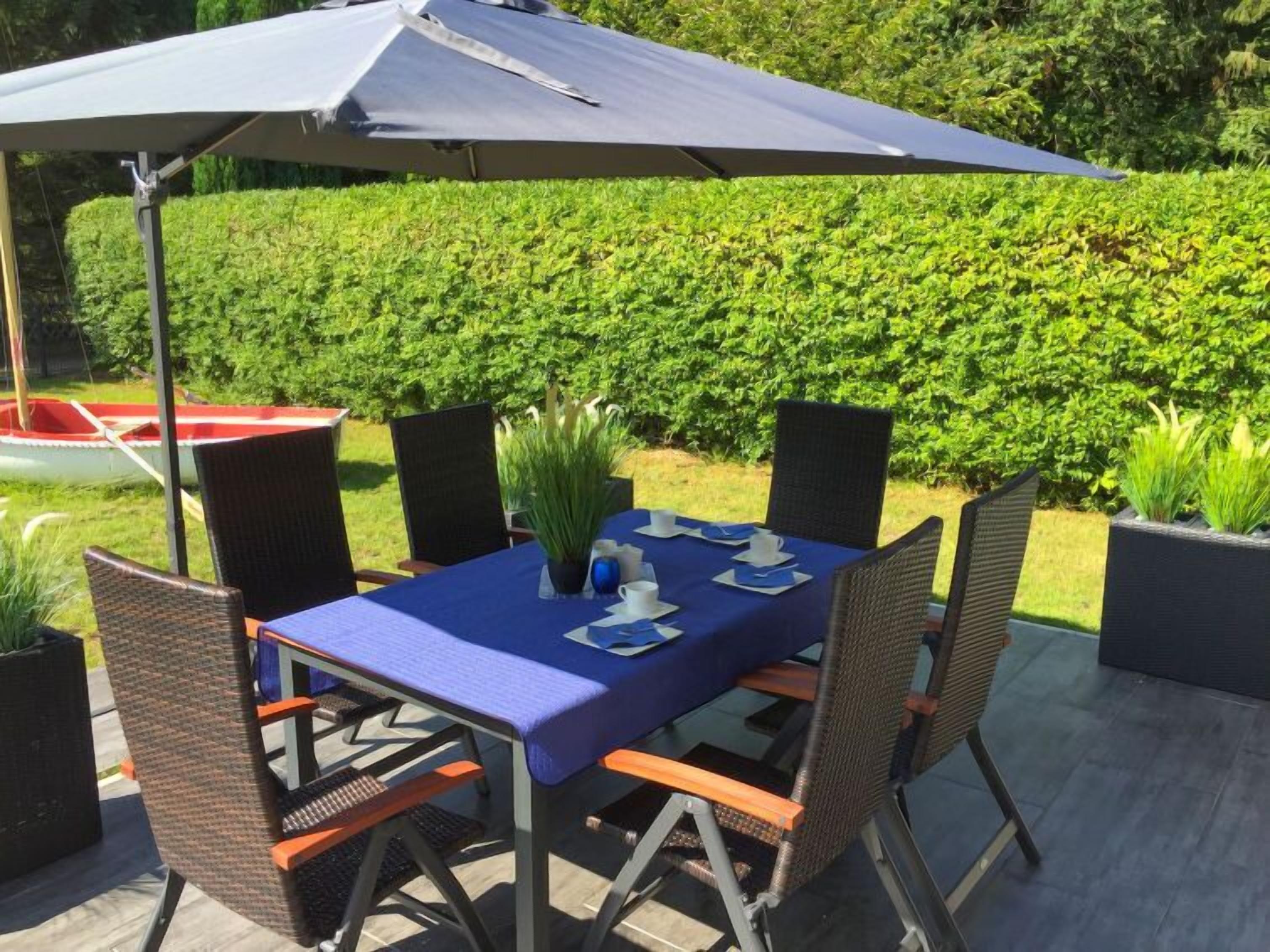 An outdoor dining area with a table set for four, surrounded by wicker chairs, under a large umbrella.