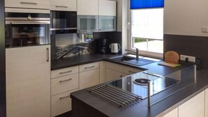 Una cucina moderna con elettrodomestici in acciaio inossidabile, un piano di lavoro nero e una finestra con persiane blu.