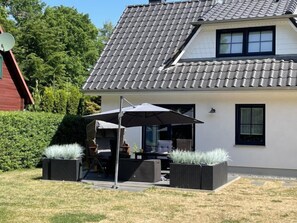 Une maison moderne avec un toit en tuiles, une terrasse dotée de mobilier d’extérieur et une antenne parabolique.