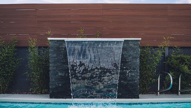 Una piscina con una cascada y una valla de madera al fondo.
