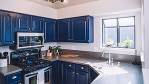 Una cocina moderna con alacenas azul oscuro, una estufa de acero inoxidable y un amplio ventanal con plantas.