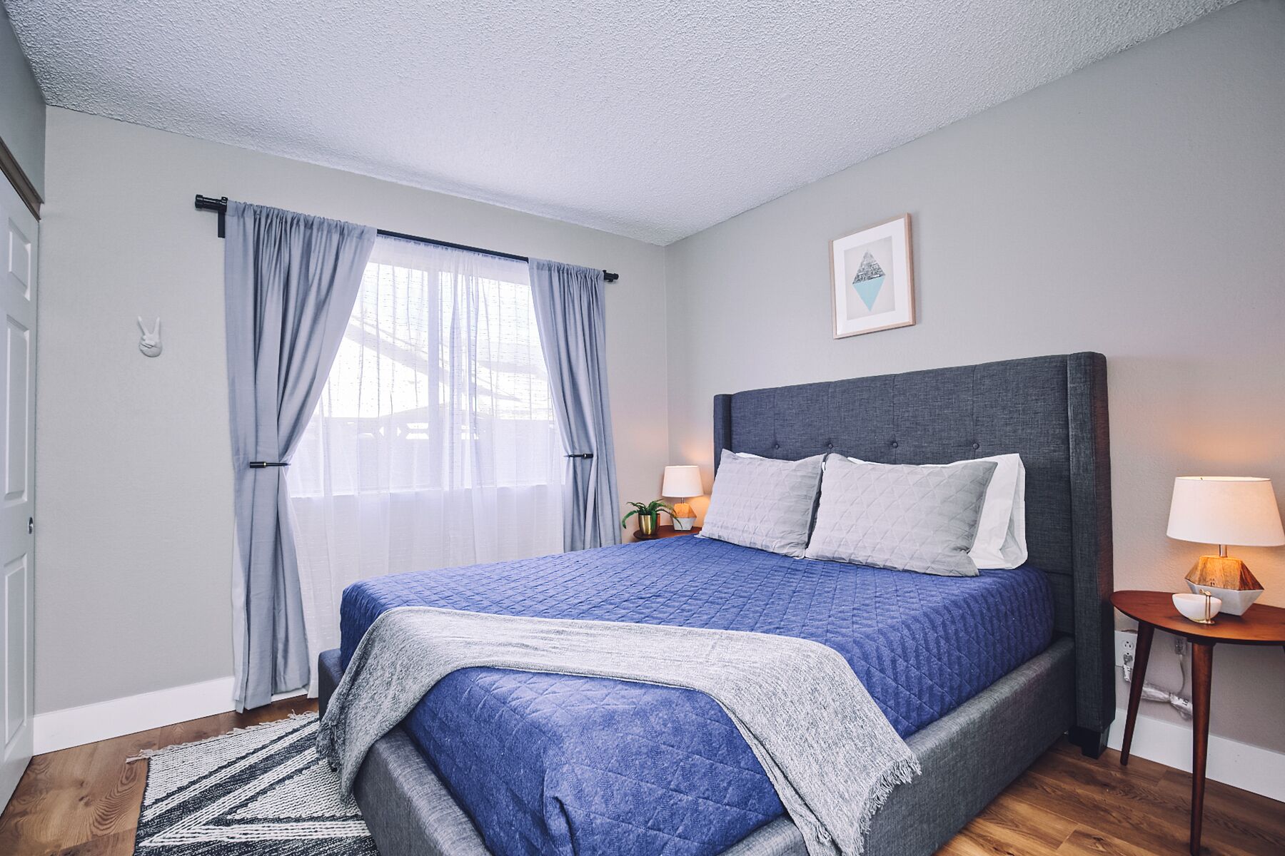 A bedroom with a large bed, a bedside table with a lamp, and a window with curtains.