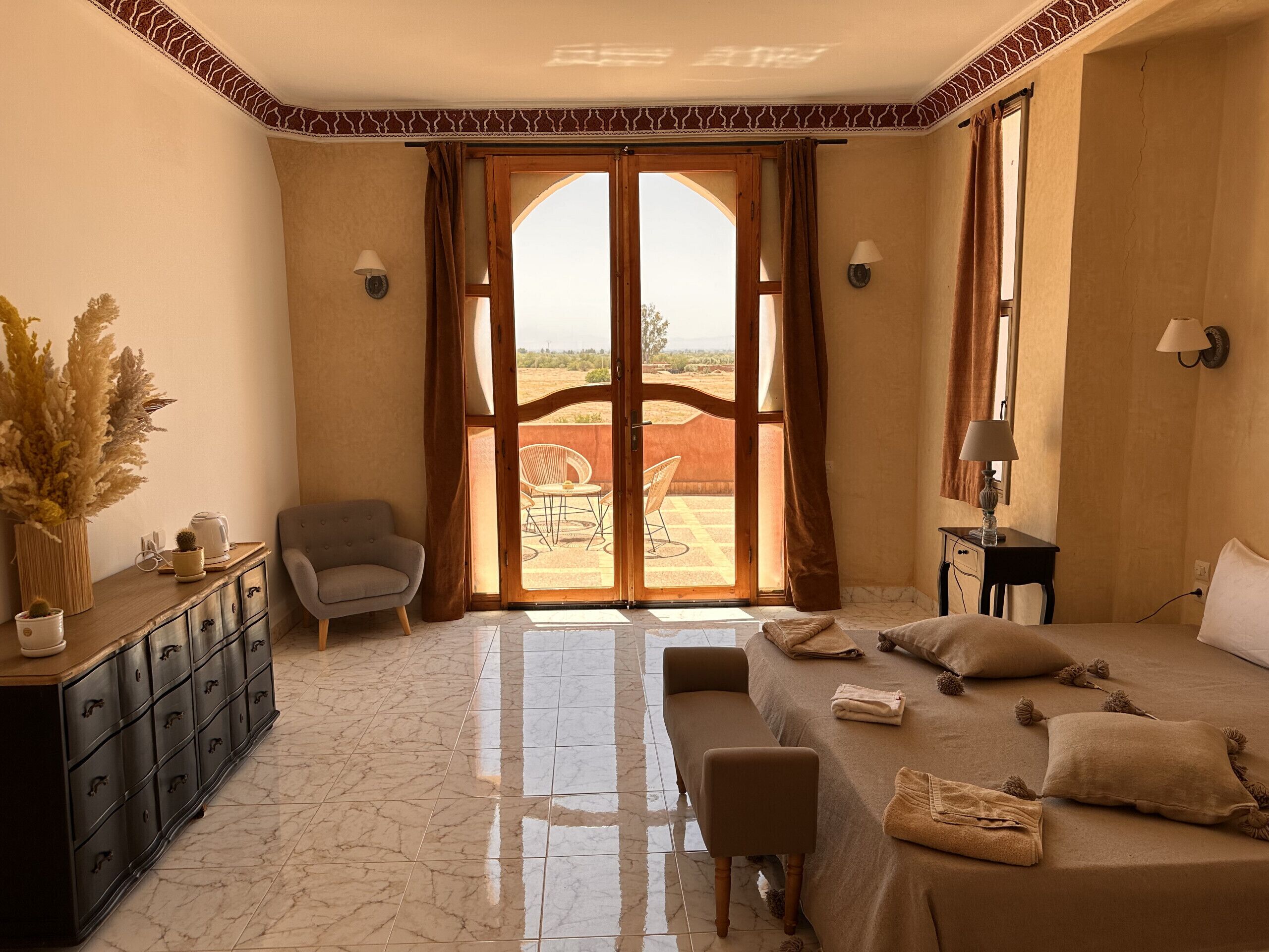 Une chambre à coucher avec un lit, une chaise, un bureau et une vue sur l’extérieur, visible à travers une grande porte.