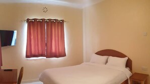 Un dormitorio con una cama, una mesita de noche de madera, un escritorio, una silla y una ventana con cortinas.