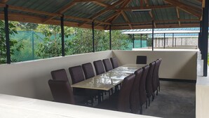 Un área de comedor al aire libre cubierta con una larga mesa y sillas, rodeada por un muro bajo y vistas a vegetación.