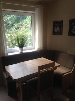 Una habitación con una mesa y sillas de madera, un ventanal con vista a la vegetación y dos cuadros en la pared.