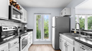 A modern kitchen with white cabinetry, stainless steel appliances, and a large window providing a view of greenery. - 3-Bed Harbor Island Home with Ocean Views, Pool Access, and Wildlife Watching! (Saint Helena Island)