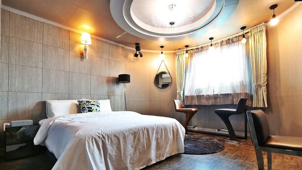 A modern hotel room with a large bed, a desk, and a chair. There is a ceiling light fixture and a window with curtains. - Number 25 Gongju Shingwan (Gongju)