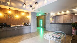 A hotel reception area with a wooden wall displaying the hotel's name, a reception desk, a waiting area with a table, and a green-lit corridor. - Number 25 Gongju Shingwan (Gongju)