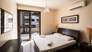 A hotel room with a bed, a desk, a chair, a balcony with a view, and an air conditioning unit. - Apt. Anna, Modern 2BDR Ayia Napa Apt. with communal pool, Close to the Beach (Ayia Napa)