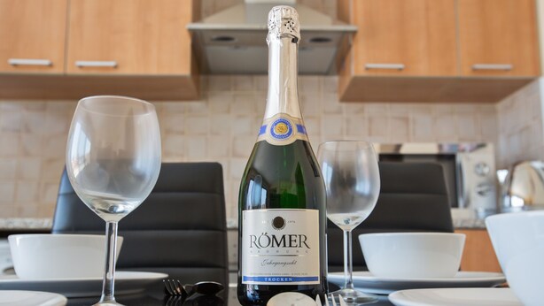 Een fles Römer champagne, twee lege wijnglazen en een eettafel gedekt met borden en bestek.