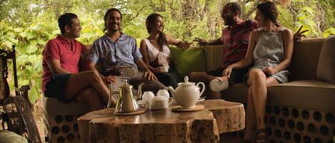 A group of people sitting on a sofa and chairs in a covered outdoor area with a table in front of them.