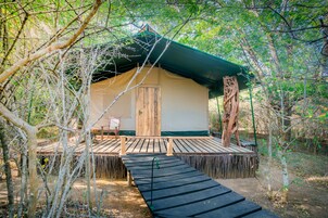 Una estructura de un nivel con terraza de madera y entrada cubierta, rodeada de árboles.