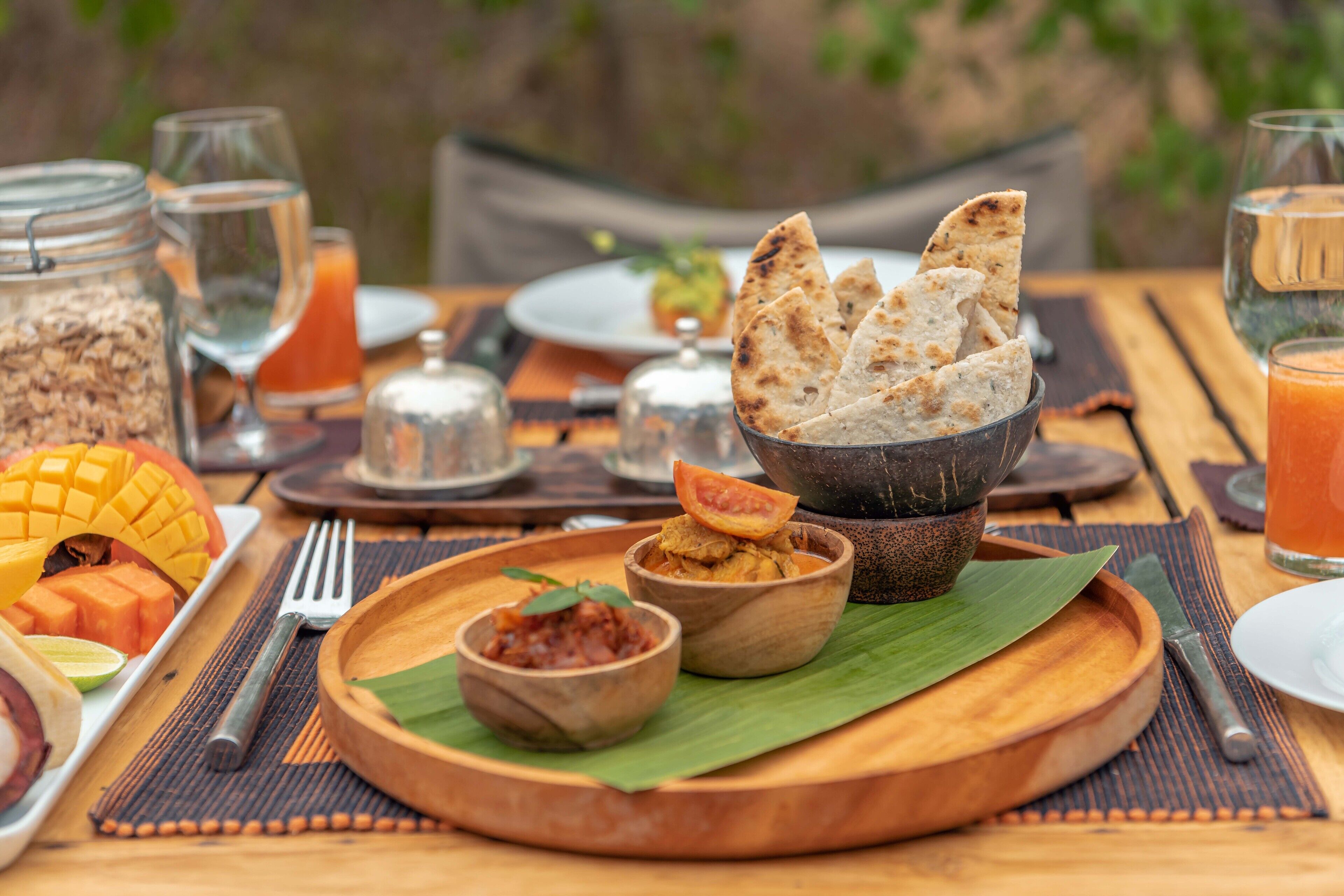 A wooden table with a variety of food items including a bowl of flatbread, a mango, and a small bowl of chutney.