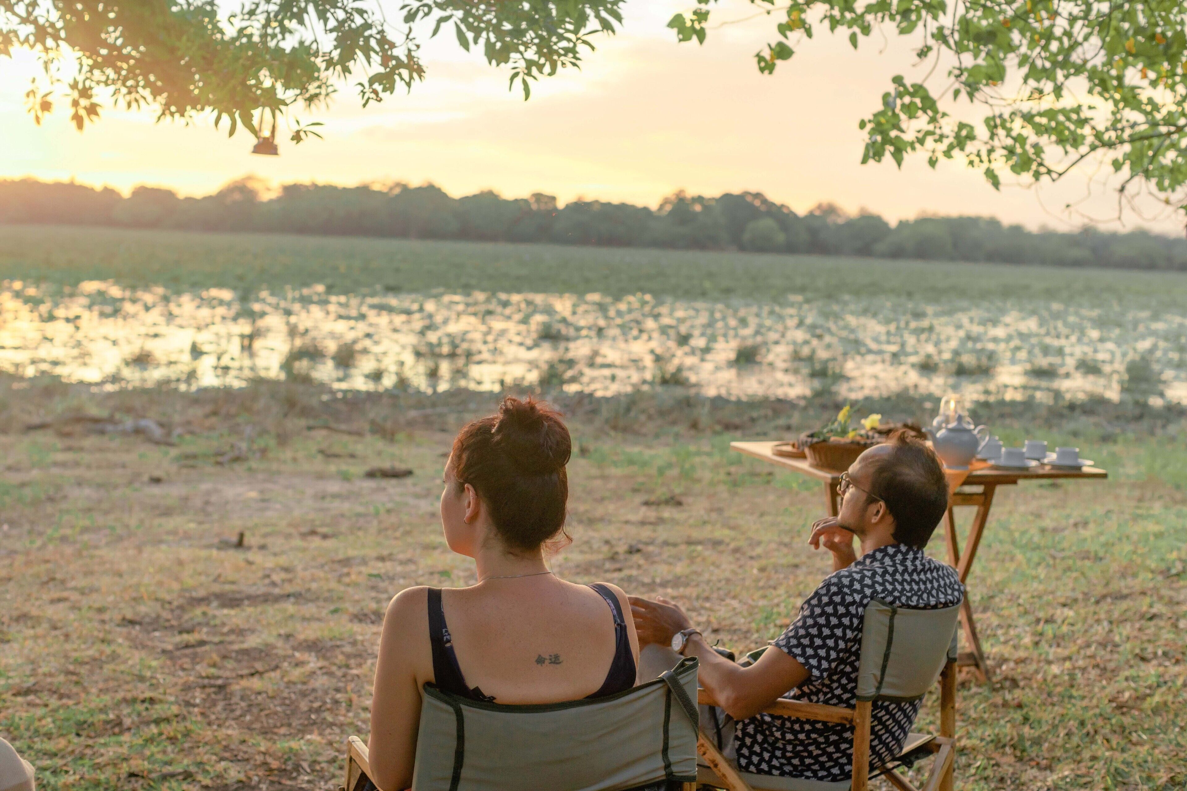Two people sitting at a table outdoors with a view of a body of water and trees in the background.