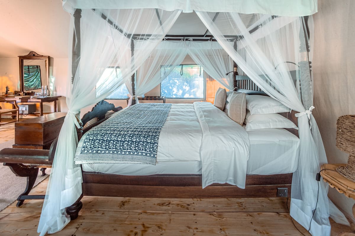 A four-poster canopy bed with a wooden frame, white bedding, and a patterned throw blanket.
