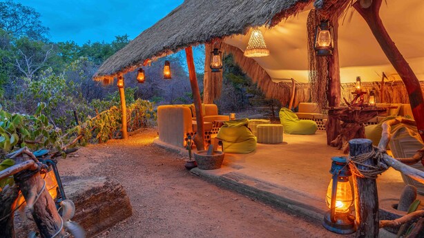 An outdoor seating area with thatched-roof structures, wooden furniture, and hanging lanterns. - Leopard Safaris Yala  (Kataragama)