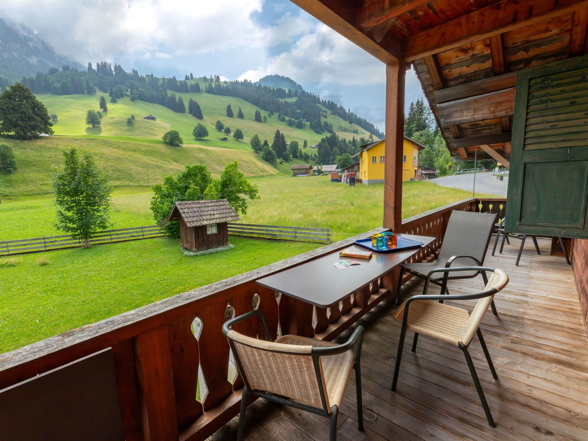 A wooden deck with a table and chairs overlooking a green landscape with houses and trees.