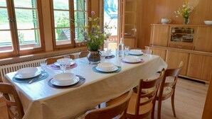 Ein Essbereich mit einem Tisch, gedeckt für vier Personen, Holzsesseln, einer Blumenvase und einem Holzschrank mit Geschirr.