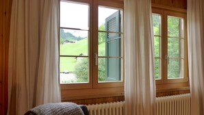 Ein Zimmer mit Holzwandverkleidung, einem Fenster mit Vorhängen, einem Heizkörper und einem Sessel mit Decke.