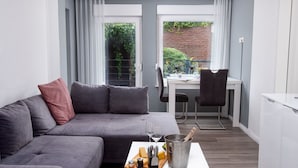 A modern living room with a grey sofa, a white coffee table with food and drink, and a kitchen area visible through an open door. - Lovely apartment for 2 guests with WIFI, TV and terrace (Norden)