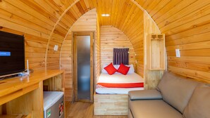 Una habitación acogedora tipo cabaña de madera con una cama, un televisor, un refrigerador pequeño y un sofá.
