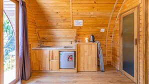 Una cabaña de madera compacta con kitchenette, que incluye un lavabo, un refrigerador pequeño y una estufa.
