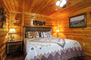 A wooden cabin room with a bed, two nightstands, a ceiling fan, a wall-mounted sign, and a framed picture.