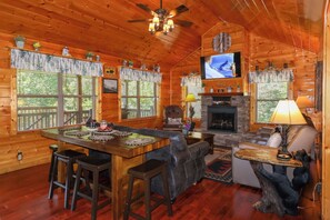 A log cabin interior with a fireplace, a television mounted above it, and a dining area with stools. - Gorgeous 5 bedroom cabin with fire pit, hot tub, mountain views, & pool table! (Pigeon Forge)
