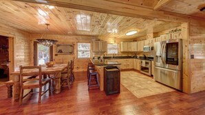Una cabaña de madera espaciosa con comedor, cocina y un amplio ventanal.
