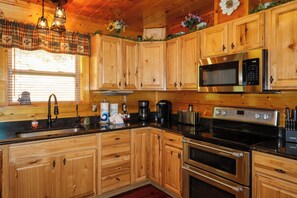 A wooden cabin kitchen with a built-in microwave, stove, and sink. - Gorgeous 5 bedroom cabin with fire pit, hot tub, mountain views, & pool table! (Pigeon Forge)