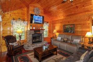 A cozy cabin interior with a fireplace, a television mounted above it, a sofa, and a coffee table. - Gorgeous 5 bedroom cabin with fire pit, hot tub, mountain views, & pool table! (Pigeon Forge)