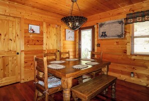 A wooden interior with a dining table, chairs, a bench, a chandelier, and a window with blinds. - Gorgeous 5 bedroom cabin with fire pit, hot tub, mountain views, & pool table! (Pigeon Forge)