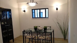 A dining area with a glass table and chairs, a small potted plant, and a window with curtains.